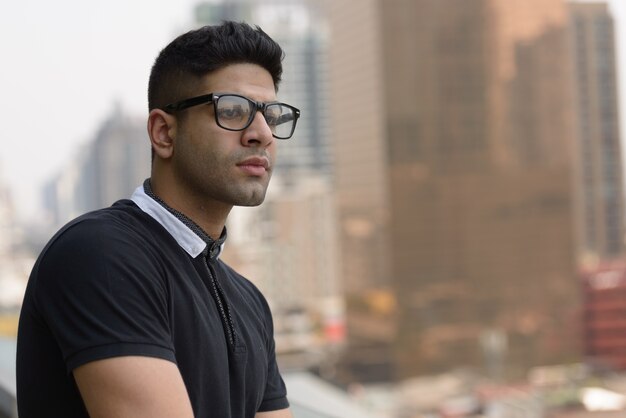 Visage de jeune bel homme indien avec des lunettes pensant dans la ville