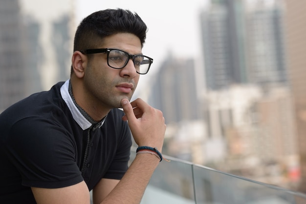 Visage de jeune bel homme indien avec des lunettes pensant dans la ville