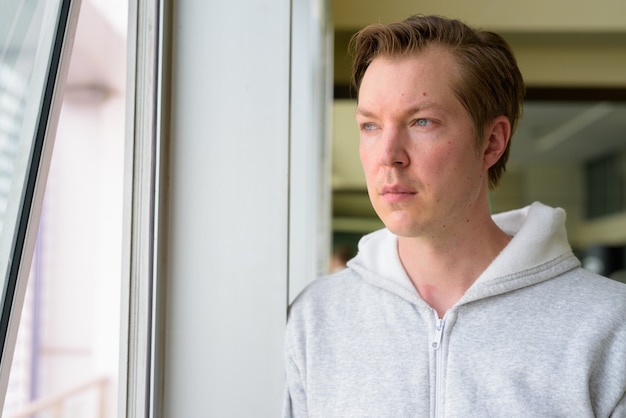 Visage de jeune bel homme pensant et regardant par la fenêtre à la salle de sport