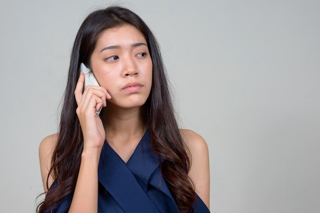 Visage de jeune belle femme d'affaires asiatique pensant tout en parlant au téléphone