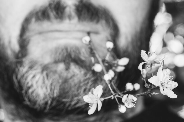 Visage masculin avec barbe et moustache avec un rameau en fleurs aux lèvres