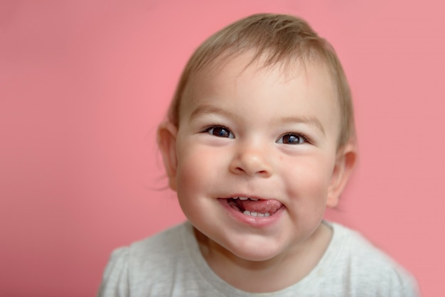 Visage mignon mignon bébé drôle visage souriant, montrant les dents et la langue, sur fond rose