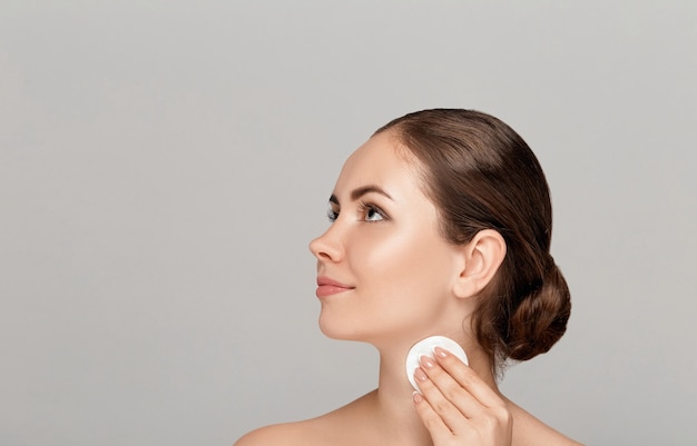 Visage de nettoyage de femme avec tampon blanc. Belle fille démaquiller le tampon de coton cosmétique blanc. Heureuse femme souriante qui décolle le maquillage de la peau du visage avec un tampon cosmétique. Soins de la peau du visage.