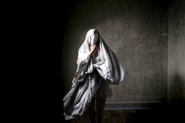 Visage obscurci d'une femme mature portant du textile contre le mur dans un endroit abandonné