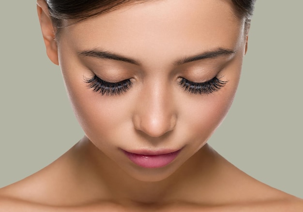 Photo visage de peau de femme avec des cils beaux yeux cheveux sains brune. baisser les yeux. fond de couleur.