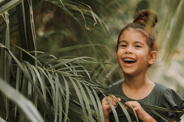 visage de petite fille entourée de feuilles tropicales Portrait en gros plan d'un enfant basané à la peau parfaite