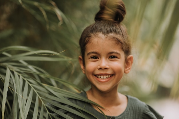 visage de petite fille entourée de feuilles tropicales Portrait en gros plan d'un enfant basané à la peau parfaite