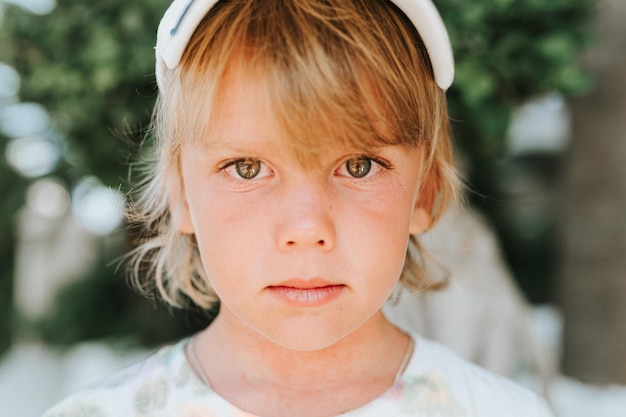 Visage portrait d'un petit garçon heureux et candide de cinq ans avec une peau allergique problématique et de longs cheveux blonds et des yeux verts sur fond de plantes vertes pendant un voyage de vacances d'été