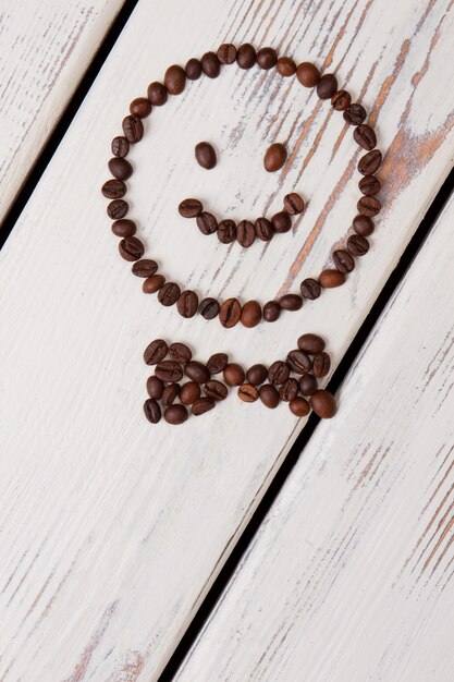 Visage souriant heureux avec noeud papillon fait de grains de café. Planches de bois blanches en surface.