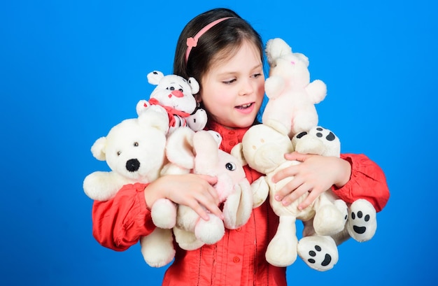 Visage souriant de petite fille avec des jouets. Enfance heureuse. Petite fille joue avec un ours en peluche. Beaucoup de jouets dans ses mains. Notion d'enfance. Passe-temps de collection de jouets. Chérir les souvenirs d'enfance.