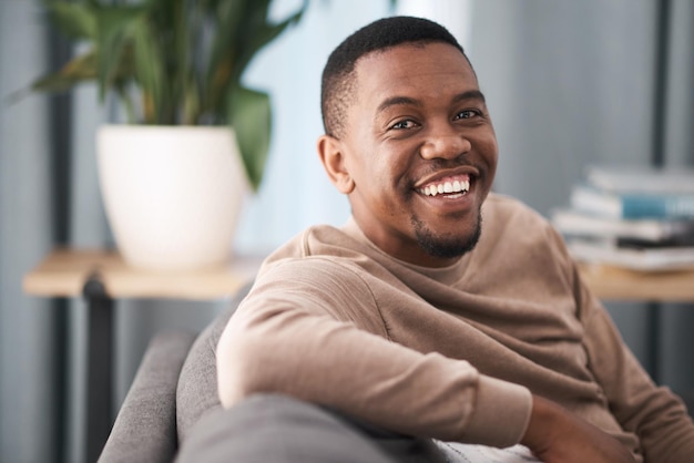 Visage souriant et portrait d'un homme noir se détendre dans un salon d'une maison en vacances ou en week-end Bonheur calme et jeune homme assis seul dans un salon dans une maison ou un appartement relaxant