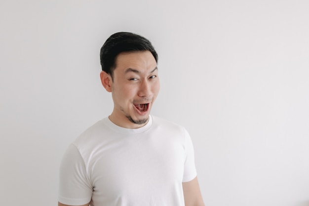 Visage de sourire drôle de sourire de l'homme en t-shirt blanc isolé sur mur blanc