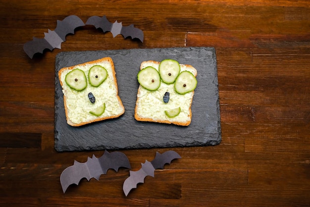 Visages De Monstres Drôles Sur Du Pain Toast Sandwich Halloween Avec Des Concombres Au Beurre De Ricotta Au Fromage Vert Doux à L'avocat Sur Des Planches De Service De Coupe Sur Fond De Bois