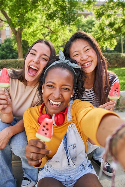 Des visages rapprochés de trois jeunes femmes multiethniques souriantes à l'extérieur mangeant de la crème glacée concept d'amitié