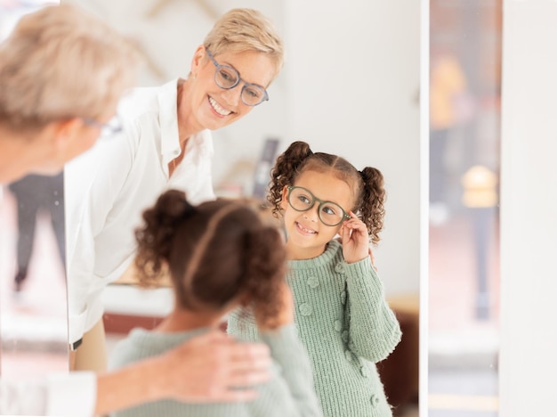 Vision des lunettes et enfants avec une fille et une femme opticienne regardant dans un miroir lors d'un rendez-vous ou d'un examen Optométrie et monture de lunettes avec un client enfant achetant des lentilles de prescription