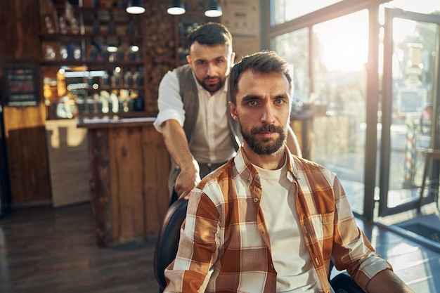 un visiteur du salon de coiffure regarde la caméra pendant que son coiffeur se tient derrière lui