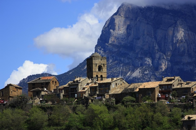 Vista de campanario, montaña y árboles en Aínsa. Pirineos, cielo azul, Torre de iglesia.