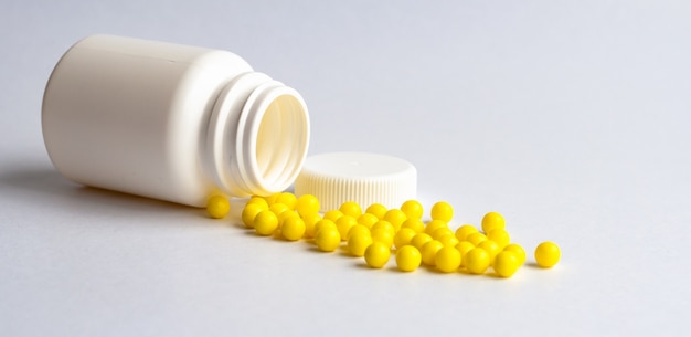 Des vitamines jaunes rondes sont versées sur une table blanche brillante à partir d'une bouteille en plastique blanche. Concept. Place pour l'étiquette. Diagnostic.
