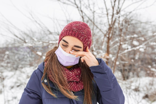 Évitez de vous toucher les yeux. Femme portant un masque facial se frottant les yeux à l'extérieur. Jeune femme touchant son œil avec une main sale. Ne touchez pas votre visage, arrêtez de propager le coronavirus