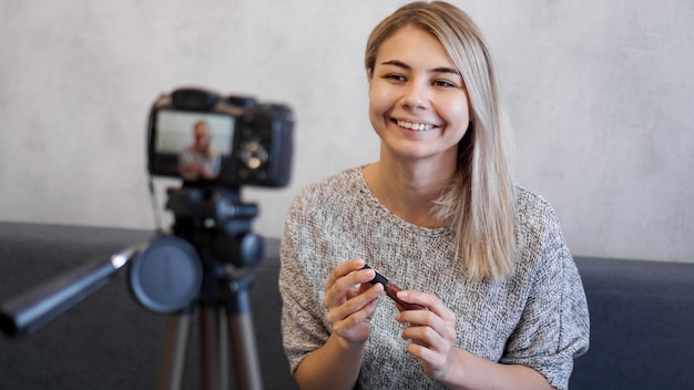 Vlogger femelle montrant le rouge à lèvres. Beauté blogueuse femme filmant tutoriel de routine de maquillage quotidien près de la caméra sur un trépied