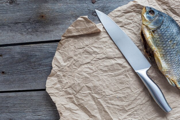 Photo vobla de poisson sec salé avec un couteau bien aiguisé sur papier craft froissé sur bois