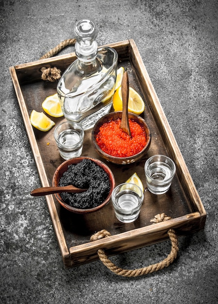 Vodka en bouteille avec du caviar noir et rouge. Sur fond rustique.