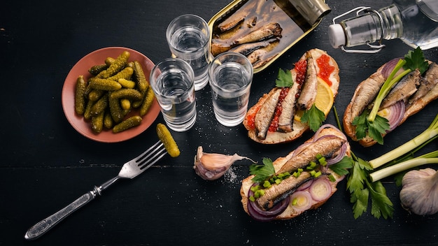 Vodka et un ensemble de sandwichs aux sprats et caviar oignon et persil sur un fond en bois Vue de dessus Espace de copie