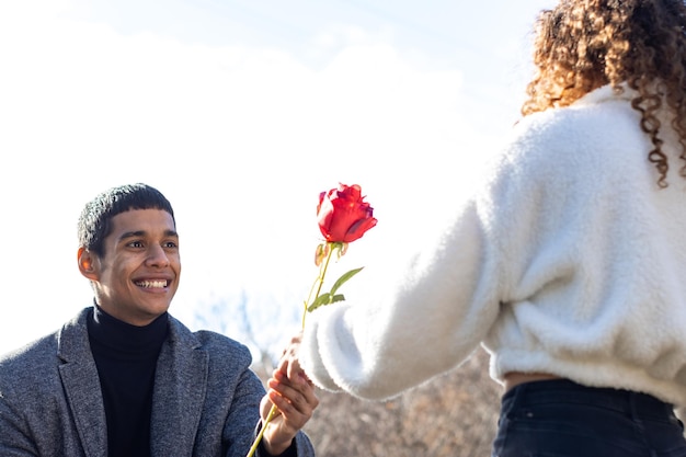 Voe arrière de femme amoureuse donnant une rose à son petit ami Jeune fille souriante amoureuse donnant une rose à son petit ami à l'extérieur