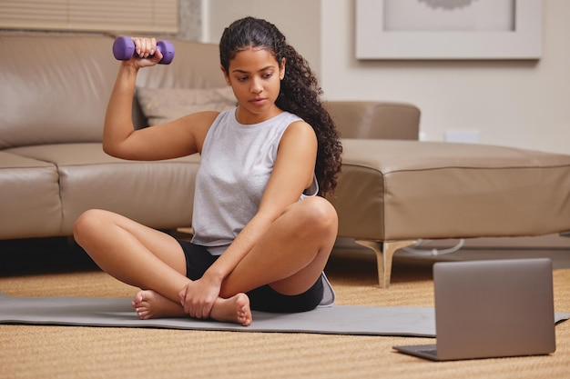 Voici des bras plus forts Photo pleine longueur d'une jeune femme utilisant son ordinateur portable pour suivre un cours de fitness en ligne dans son salon