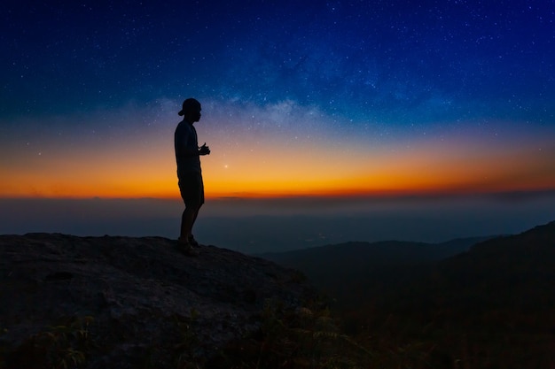 Voie Lactée. Ciel nocturne coloré avec étoiles et silhouette d'un homme debout sur la pierre. Bleu laiteux w