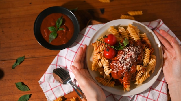 Voir ci-dessus Mains féminines tenant une assiette de pâtes fusilli sur une table à manger en bois Cuisine italienne