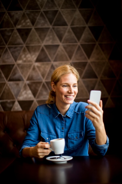 Voir à la jeune femme assise au café, en utilisant le téléphone et boire un café