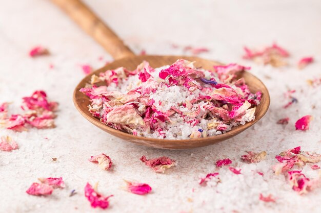 Voir le sel avec des pétales de fleurs séchées dans une cuillère en bois sur une table en marbre rose