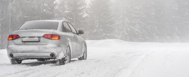 Voiture argentée garée sur une route d'hiver couverte de neige, arrière-plan flou d'arbres, vue de derrière