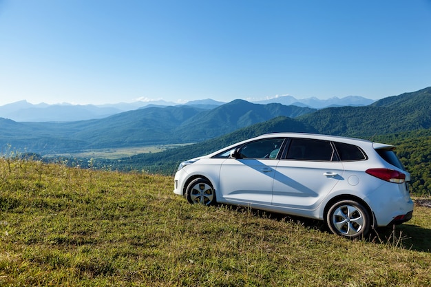 Une voiture blanche se dresse sur une pente sur fond de belles montagnes verdoyantes à Adygea