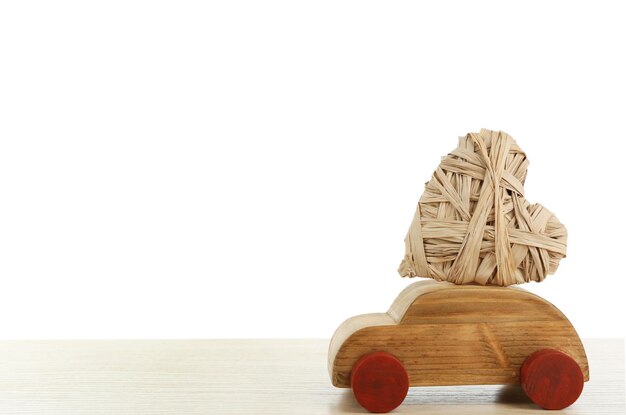 Voiture en bois avec un coeur en osier sur une table en bois blanche