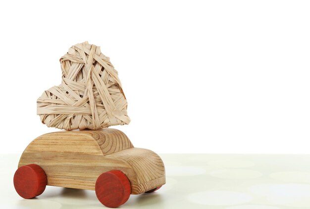 Voiture en bois avec un coeur en osier sur une table en bois blanche