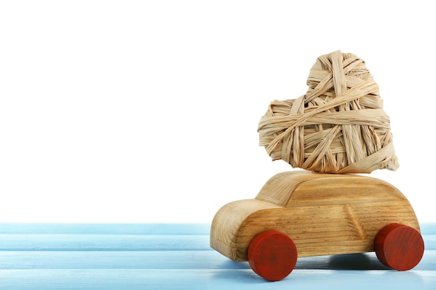 Voiture en bois avec un coeur en osier sur une table en bois bleue