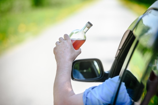 Voiture de bouteille d'alcool et concept de conduite en état d'ébriété la personne tient en main une bouteille de boisson alcoolisée au volant de la voiture