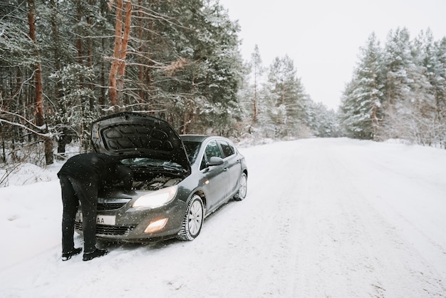Une voiture avec un capot ouvert sur le fond d'une forêt d'hiver
