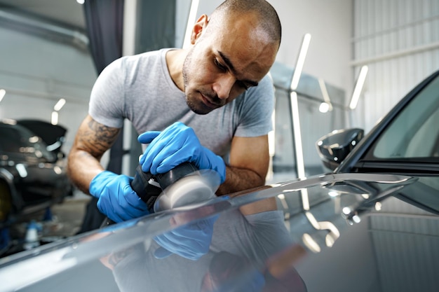 Voiture détaillant les mains des hommes avec une polisseuse orbitale dans un atelier de réparation automobile