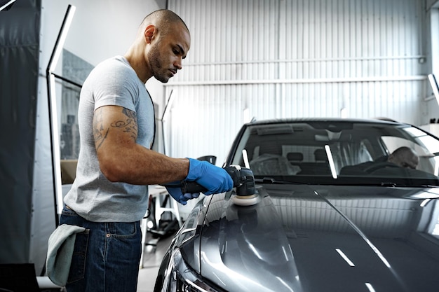 Voiture détaillant les mains des hommes avec une polisseuse orbitale dans un atelier de réparation automobile