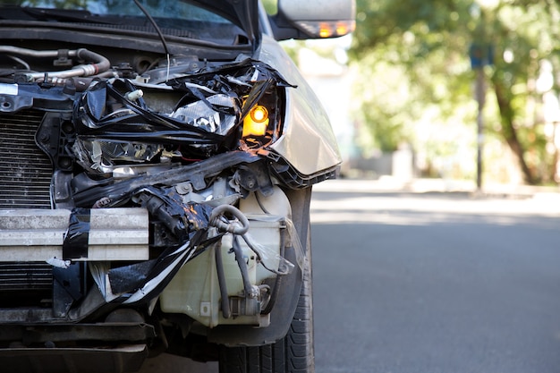 Voiture détruite dans un accident de la circulation sur la route de la ville avec espace de copie. Phare auto avant cassé brisé, capot cabossé sans pare-chocs sur accident de voiture gris. Assurance vie et maladie automobile.