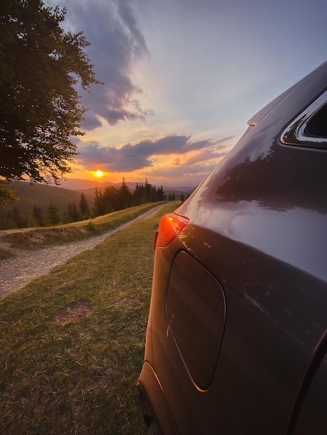 Voiture grise près d'un grand vieux hêtre dans les montagnes au coucher du soleil