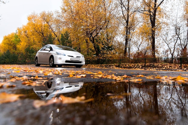 Voiture hybride blanche sur la route d'automne en jour de pluie