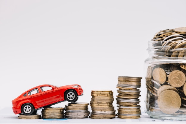 Photo voiture jouet monter sur la pile croissante de pièces de monnaie près du pot de pièces de monnaie sur fond blanc