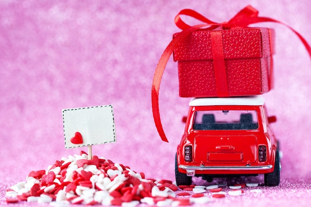 Photo voiture jouet rouge livrant transportant sur la boîte-cadeau de toit et plateau vide sur un mur rose brillant pour le concept de la saint-valentin.