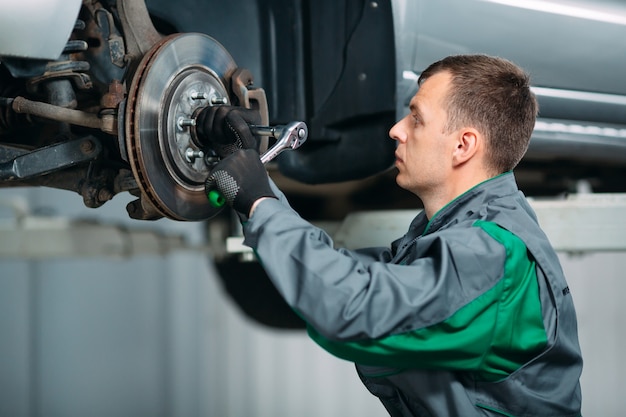 Voiture levée en service automobile pour la réparation et le travailleur répare la roue