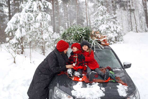 Une voiture et une maman et ses filles au milieu de la forêt avec un sapin de Noël et des cadeaux