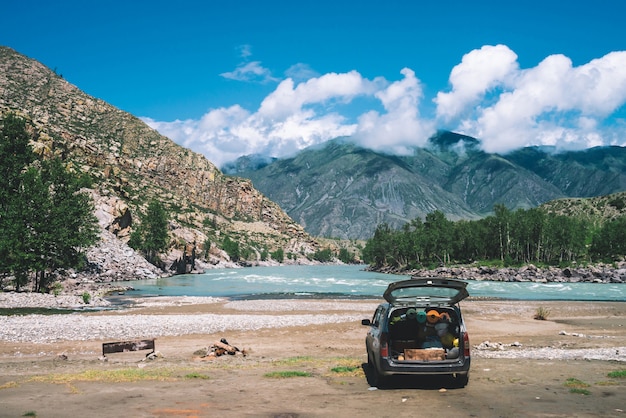 Voiture ouverte grand coffre près d'une rivière de montagne aux eaux turquoises.